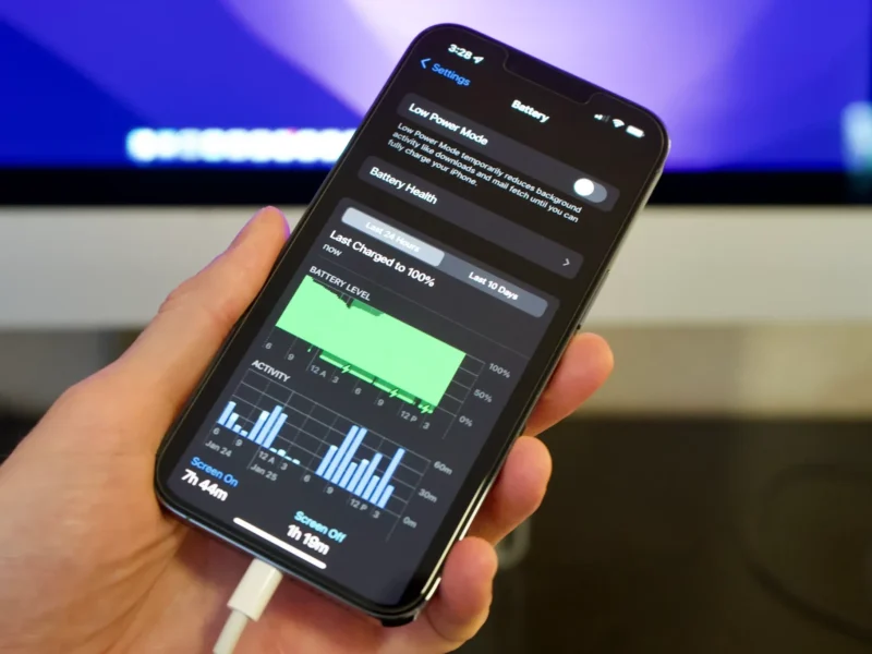 Person fixing iPhone 15 battery drain issue with phone settings and charger beside